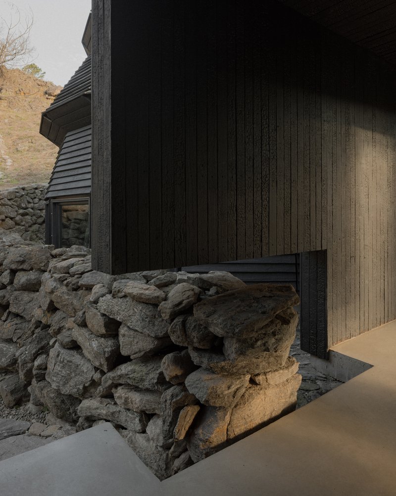 Exterior corner detail with charred vertical timber cladding meeting an exposed fieldstone foundation