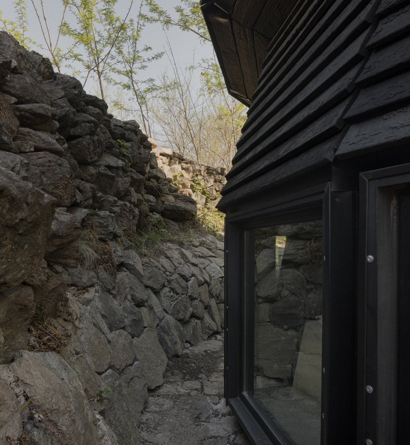 Glass door in blackened wood facade opening onto a narrow courtyard carved from volcanic rock