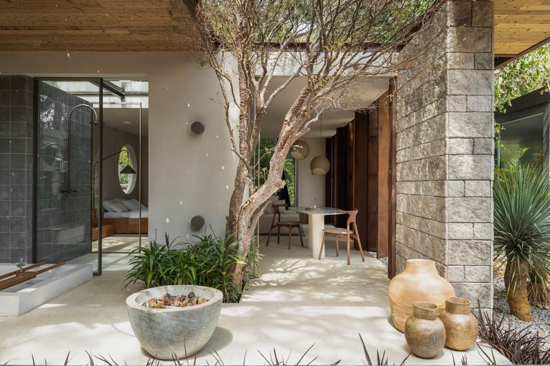 Interior courtyard with mature tree, concrete pavers, stone block column and ceramic vessels in afternoon light