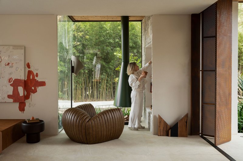 Living room with perforated metal screen and person at full-height window overlooking bamboo garden
