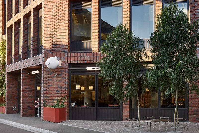 Street view of the red brick facade with ground-floor cafe storefront and a weeping willow