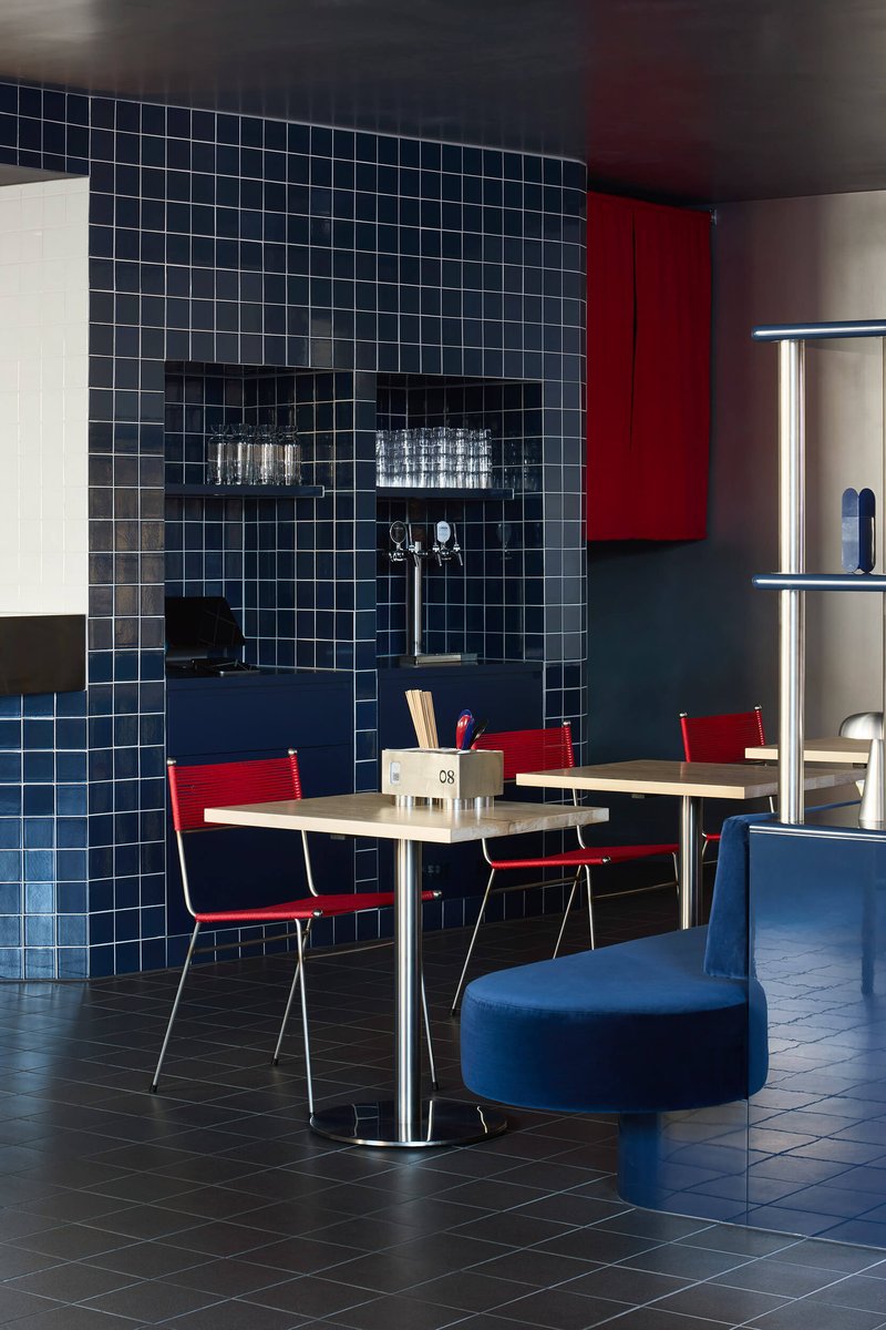 Navy tiled wall with recessed shelving niche beside tables and red cabinet panels