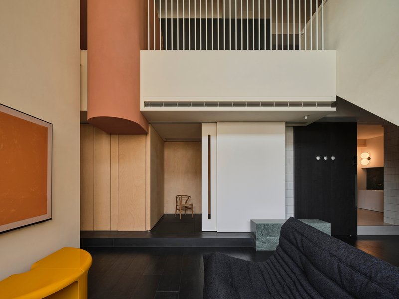 Double-height living space with vertical timber slat balustrade and suspended cylindrical terracotta duct in afternoon light