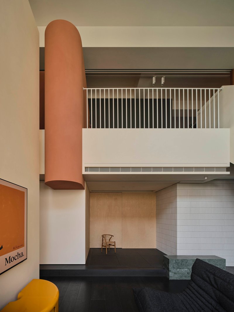 View of cylindrical terracotta column rising through the interior alongside white metal balustrade and wood paneled walls