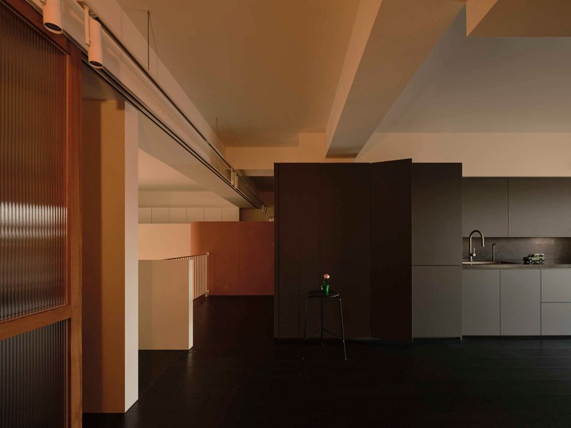 Ribbed glass sliding partition and freestanding black partition wall flanking kitchen with stepped ceiling beams above