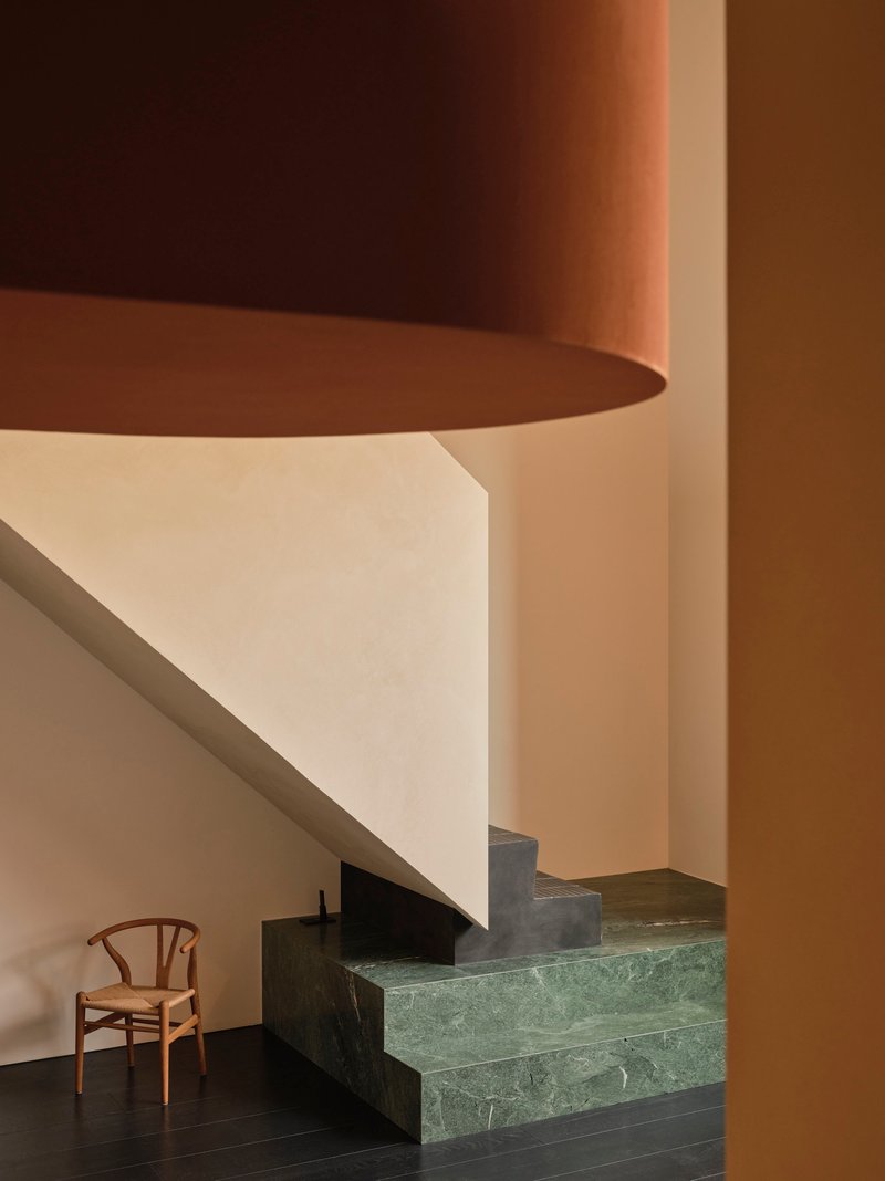 Close-up of green marble stair treads below curved white soffit and cylindrical terracotta column in warm light