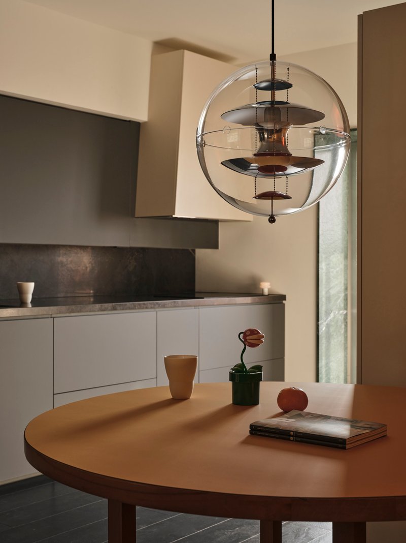 Spherical glass pendant light with layered metal discs suspended above a round dining table