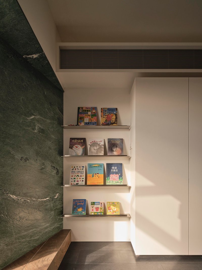 Corner nook with floating shelves displaying books beside a green marble wall