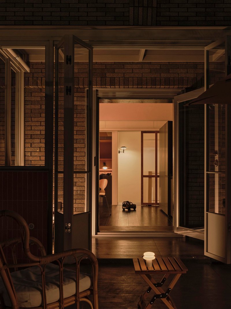 Open timber framed doors leading from dark brick courtyard into illuminated interior corridor at evening