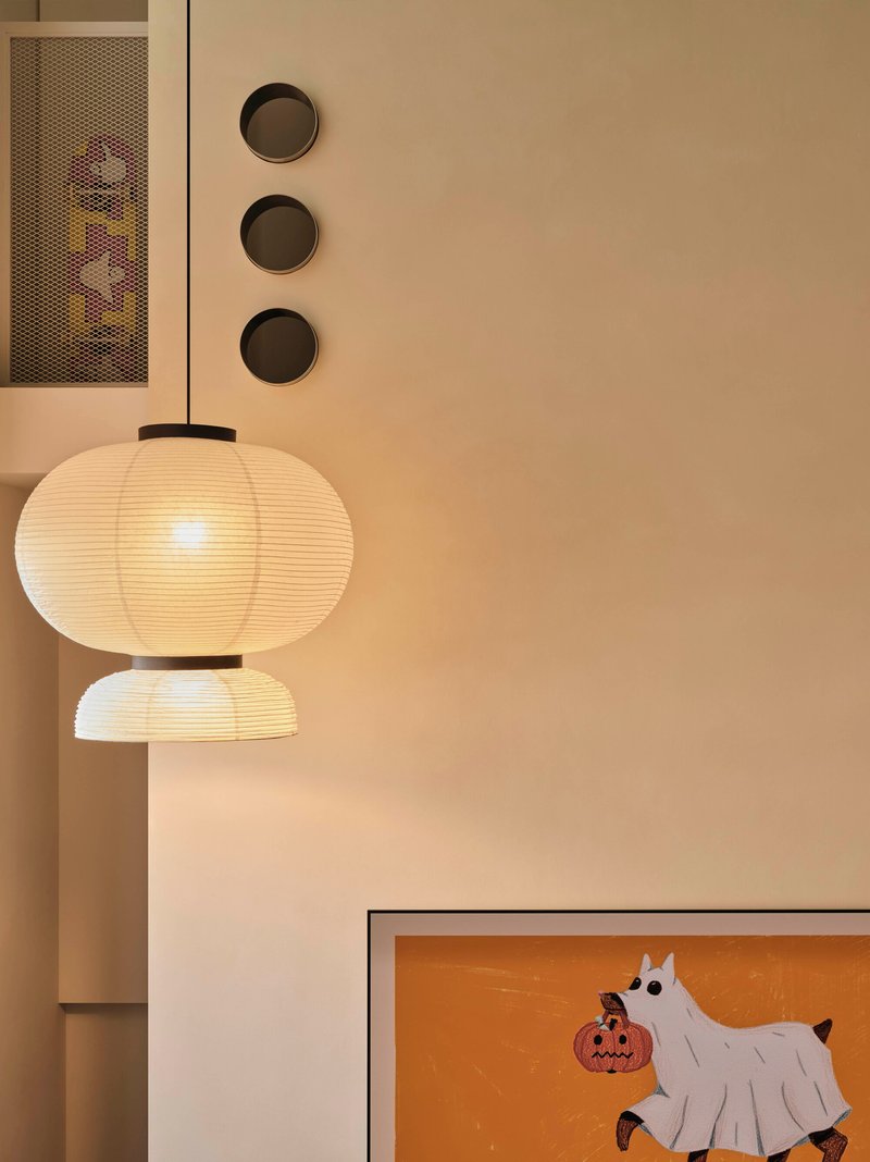 Paper lantern fixture beside a wall with three circular recesses and a framed drawing below