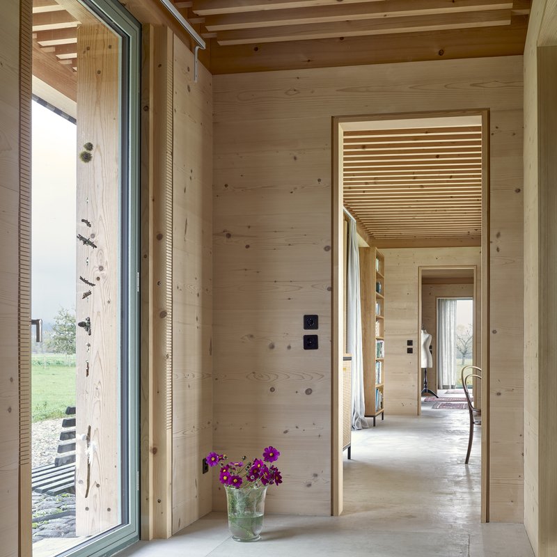 View through aligned doorways showing timber-clad walls, slatted ceiling inserts, and purple flowers on the floor