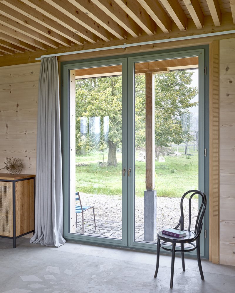 Glazed door opening to gravel terrace with a bentwood chair beneath an exposed timber beam ceiling