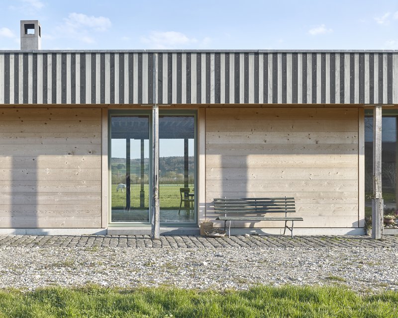 Facade detail showing vertical striped metal cladding above concrete walls with glazed doors and steel columns