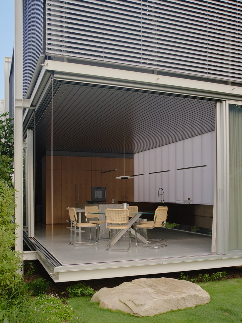 Kitchen pavilion with fully retracted corner glazing and horizontal louver facade above