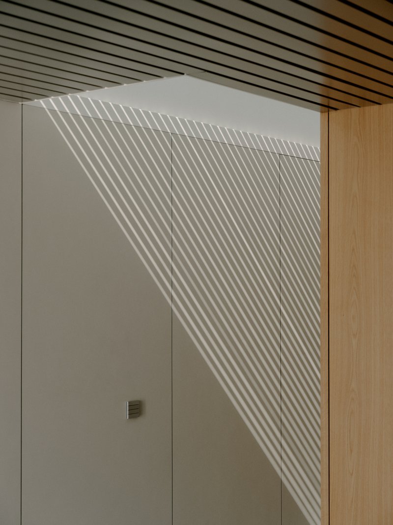 White wall with linear shadow pattern from slatted ceiling illumination falling across doorway