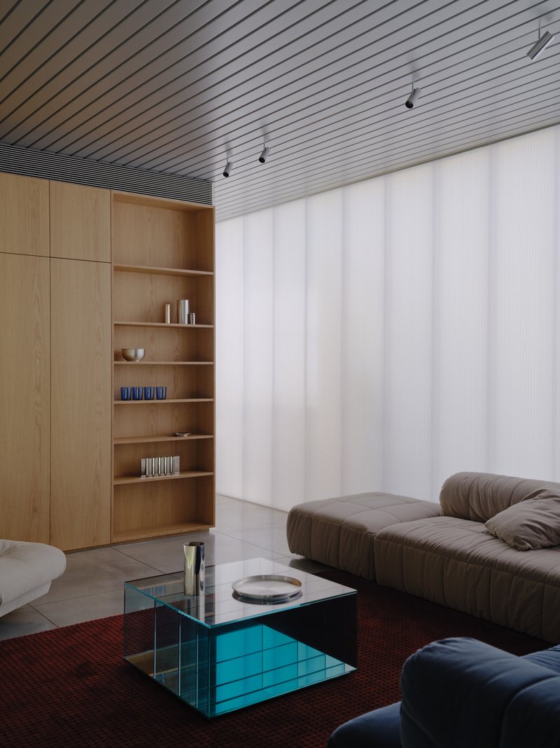 Living room with slatted wood ceiling, built-in shelving, and translucent vertical panel system