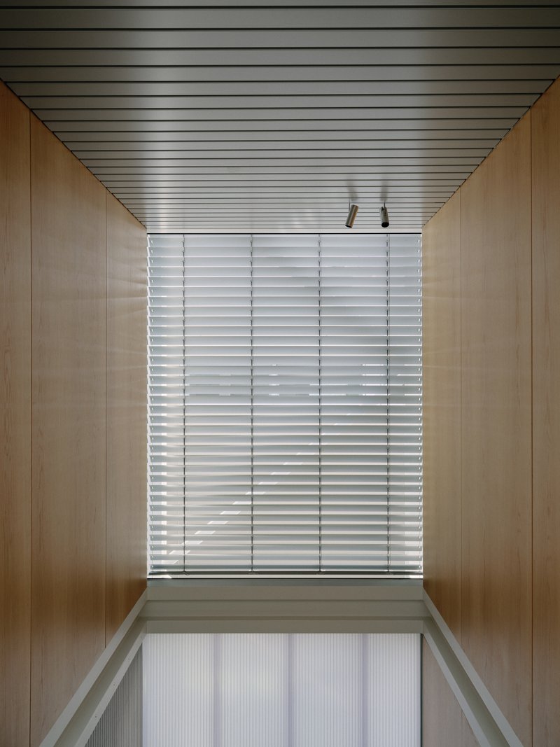 Wood-lined corridor with slatted metal ceiling and horizontal louvered window at end
