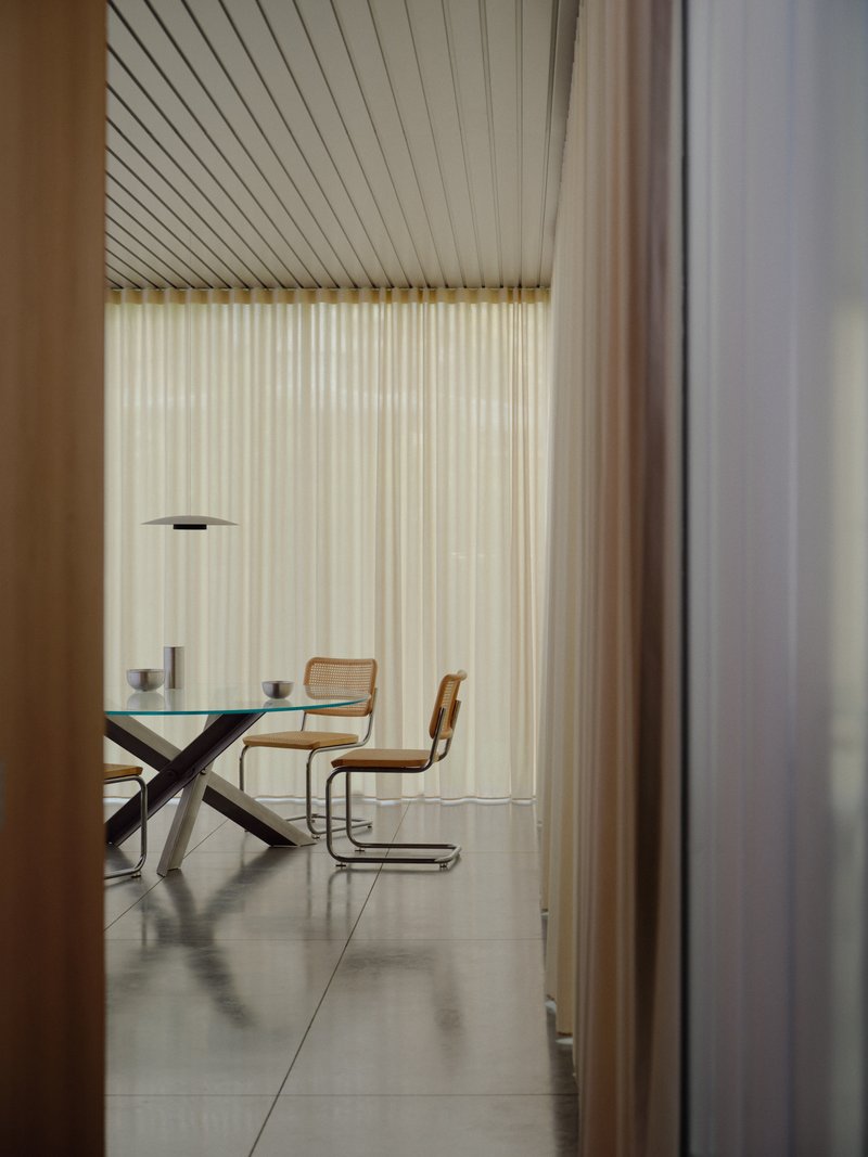 Dining room view through doorway with slatted ceiling and cantilever table in soft natural light