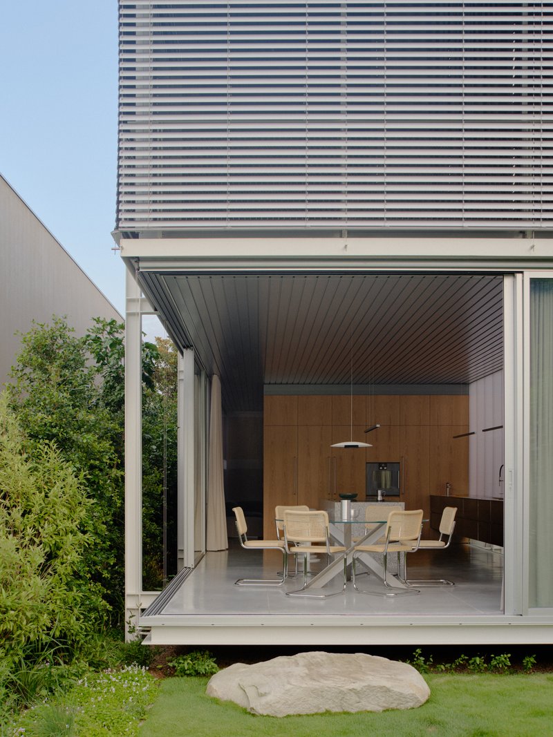Exterior view of open pavilion with dining area extending to lawn with large boulder