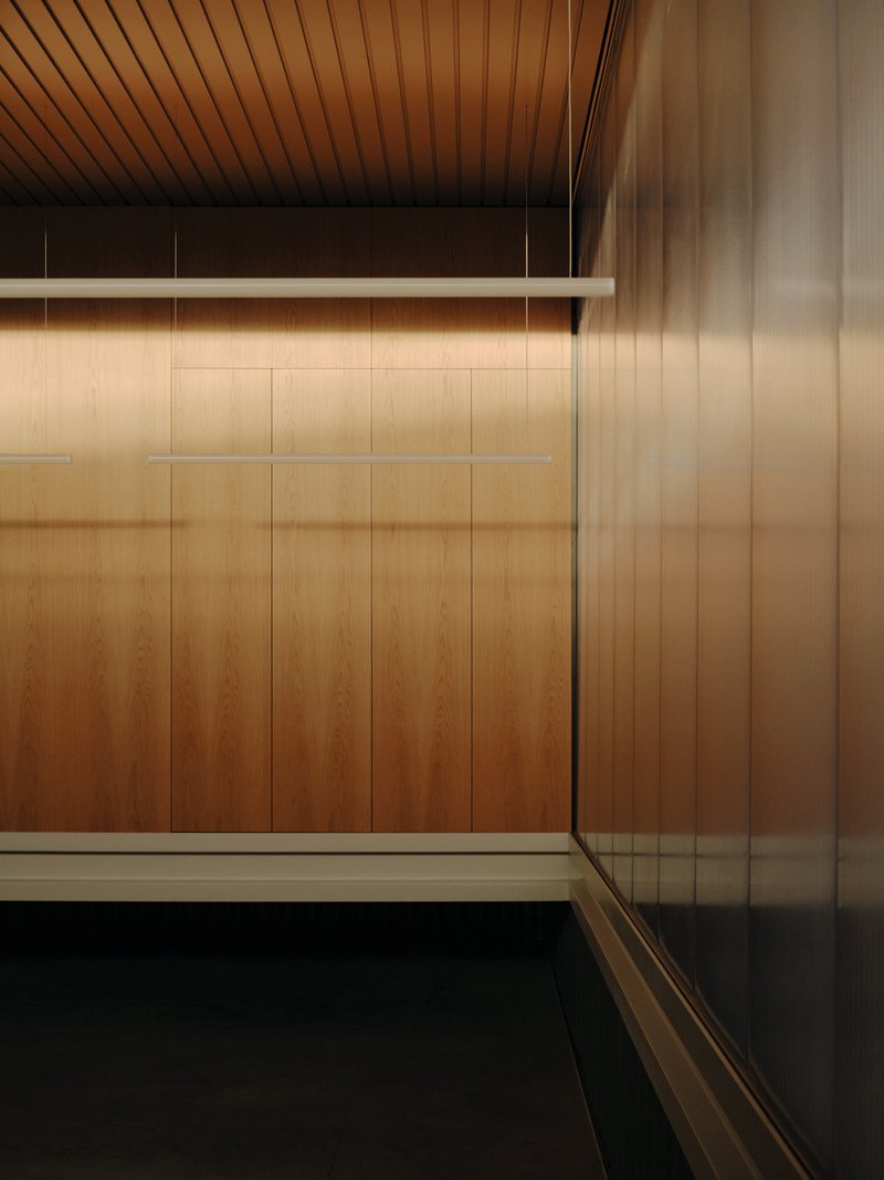 Interior corner with timber-paneled walls and slat ceiling meeting a translucent curtain beside black flooring