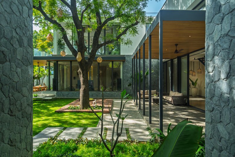 Courtyard with stone-clad volumes, glazed walkways, and an existing tree preserved in the lawn