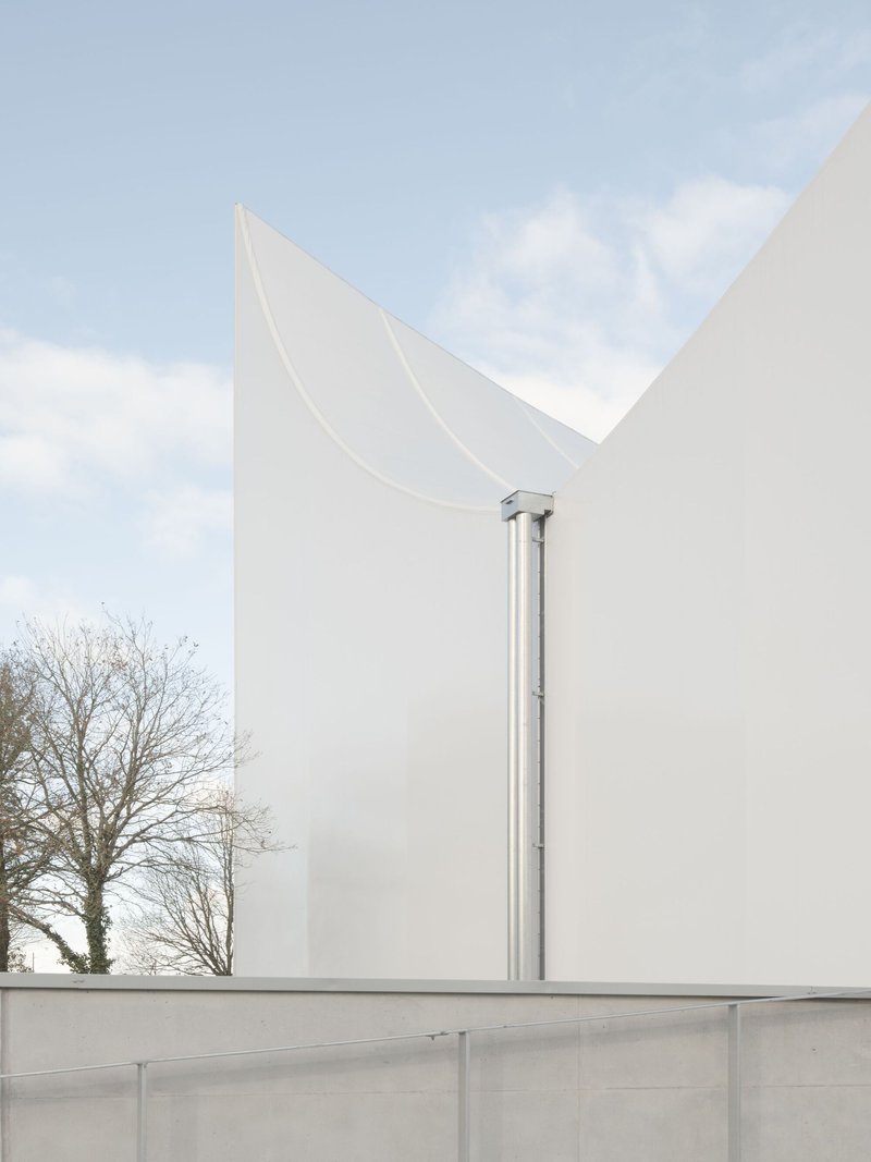 Stainless steel exhaust stack between two white curved roof peaks under cloudy sky