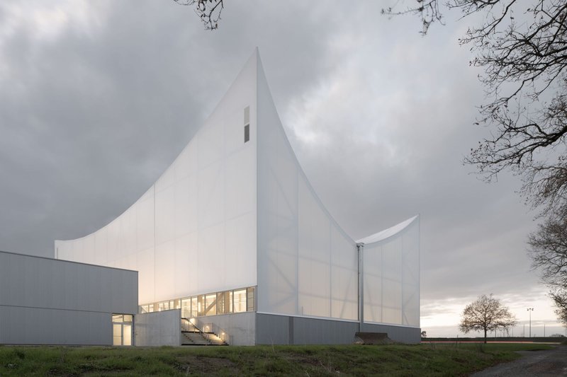White folded membrane facade with illuminated ribbon windows at dusk under overcast skies