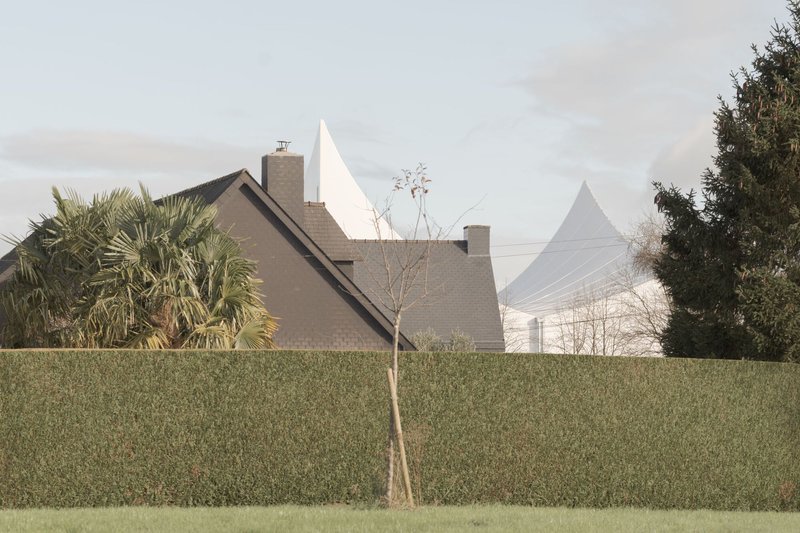 Distant view of the peaked white roof rising above residential hedges and a young tree