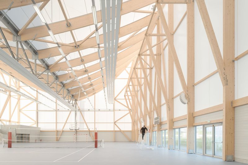 Interior sports hall with exposed laminated timber trusses and a figure walking along the volleyball court