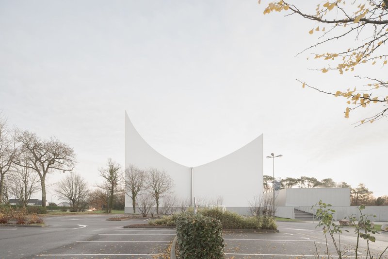 White curved roof rising above a parking lot framed by bare winter trees