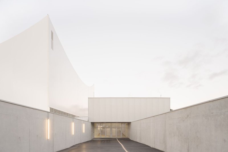 Concrete courtyard entrance with glazed doors and vertical strip lighting at dusk
