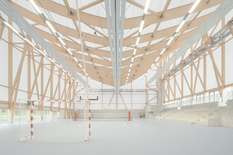 Interior sports hall with exposed timber truss roof structure and bleacher seating