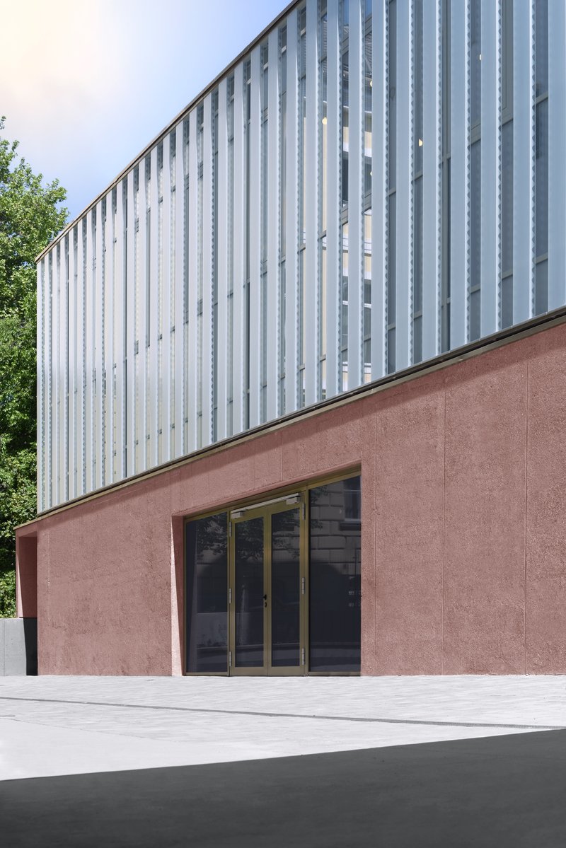 Two-story volume with pink stucco base and vertical white metal cladding beside green trees