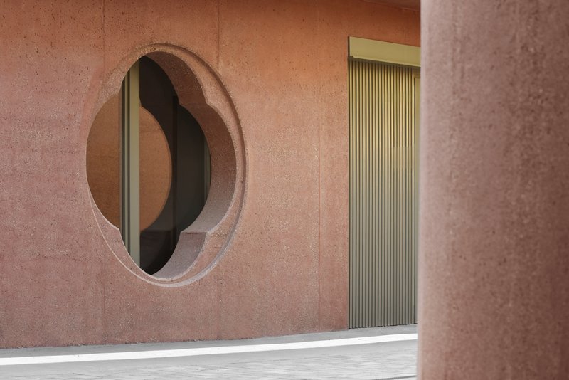 Pink rendered facade with an organic oval window and fluted green doorway in bright sunlight