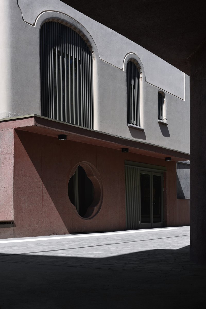 Street view of pink and white stucco facade with oval window and cantilever overhang in harsh sunlight