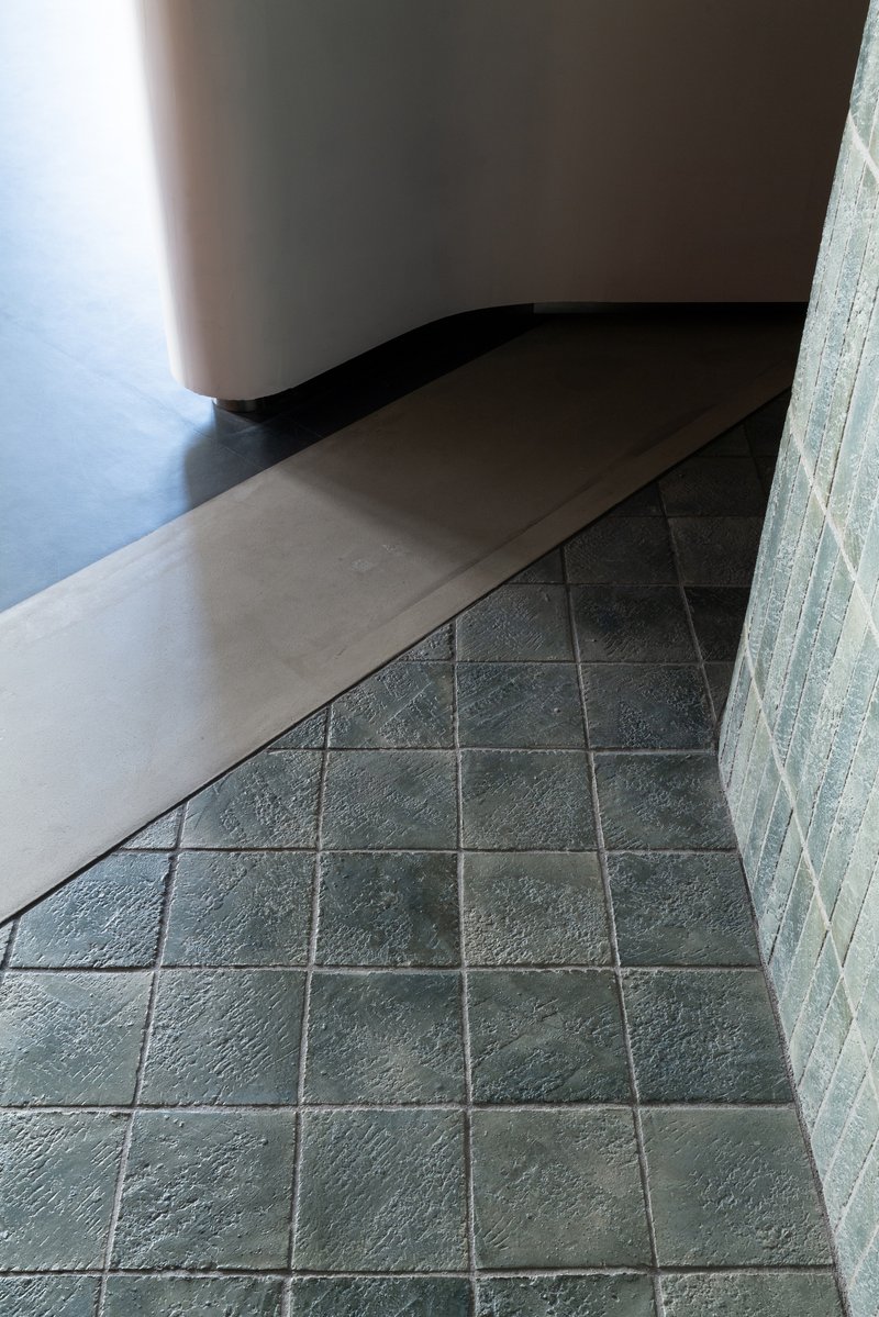 Curved white bench meeting dark tile floor along textured concrete block wall