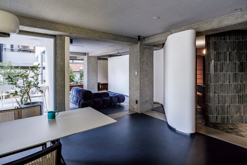 Open living area with exposed concrete beams and curved white partition separating spaces with terrace beyond