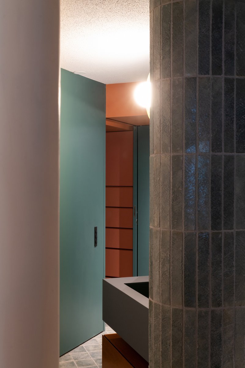 Doorway framed by teal wall panels and dark vertical tile leading to terracotta shelving beyond