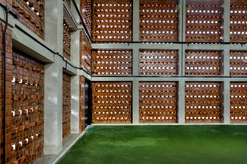 Perforated brick screen wall with concrete frame grid and green turf floor below
