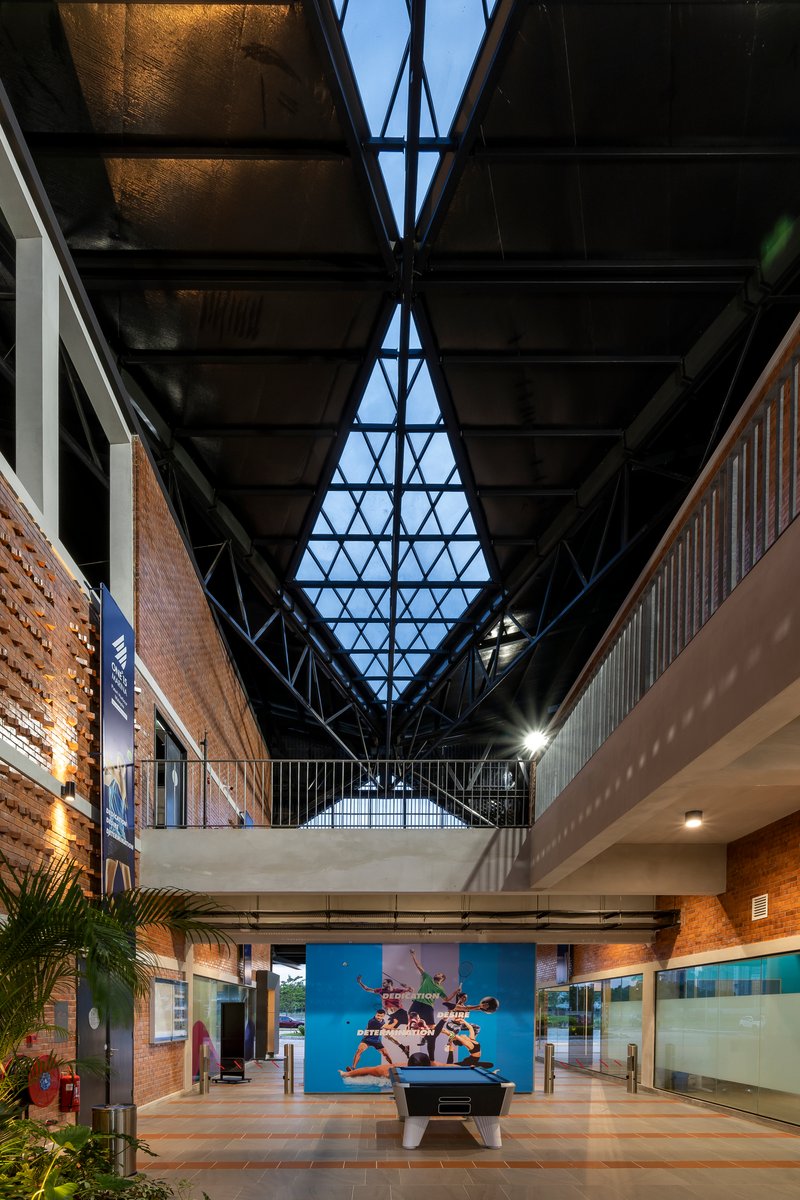 Central atrium with triangular skylight framed by black steel trusses at dusk