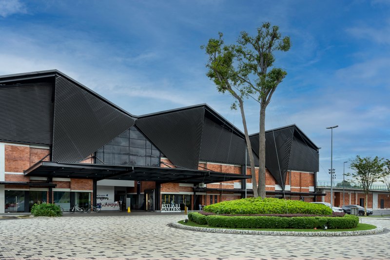 Front plaza with brick base, corrugated metal gable roofs, and a single tree under blue sky