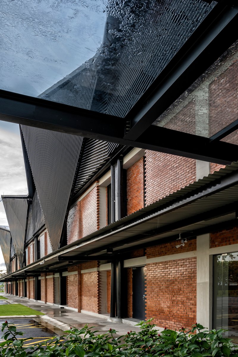 Covered walkway with black steel beams, corrugated metal canopy, and brick facade along glass storefronts