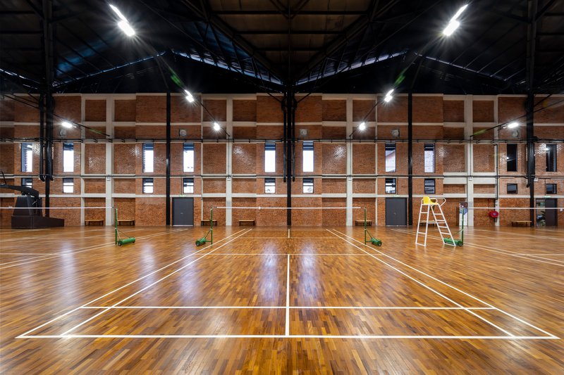 Indoor sports hall with timber floor, exposed steel roof trusses, and brick perimeter walls at night