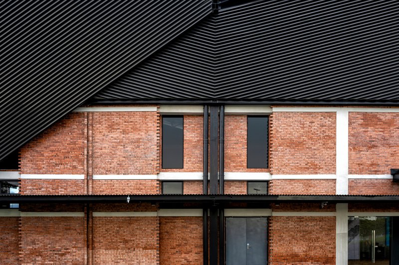 Facade detail showing brick walls with horizontal banding beneath ribbed metal roof planes