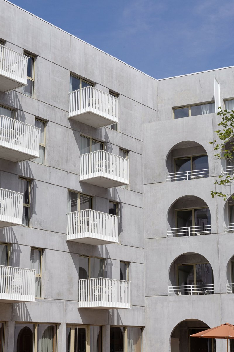 Courtyard view showing concrete balconies with vertical railings facing arched openings across the space