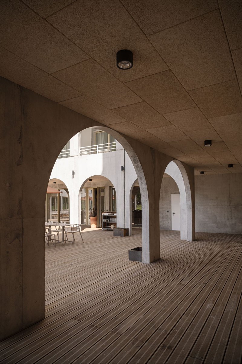 Arcade with rounded concrete arches, cork tile ceiling, and timber decking opening to a sunlit courtyard