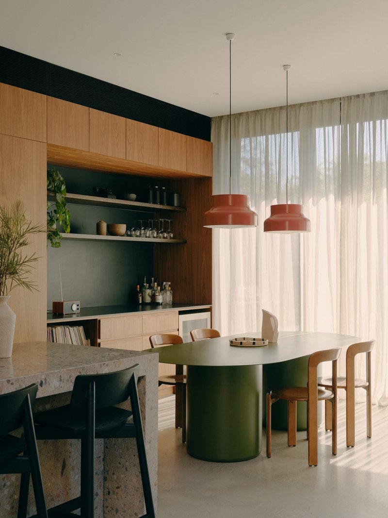 Dining space with timber cabinetry and terrazzo table beneath sheer curtains in soft daylight