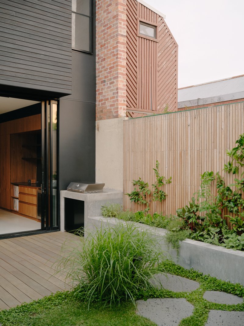 Courtyard with concrete stepping stones through lawn leading to planted beds and timber screening fence