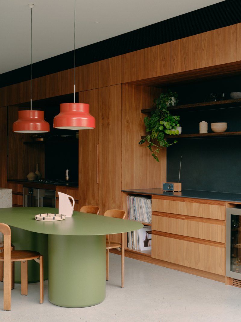 Dining area with green cylindrical table, timber joinery wall and orange pendant lights above