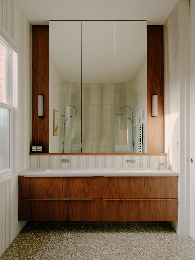 Floating walnut vanity with dual sinks and full-height mirrored cabinet in a tiled bathroom